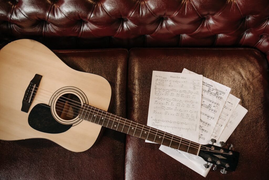 A flat lay of an acoustic guitar with sheet music on a leather sofa, perfect for music lovers.